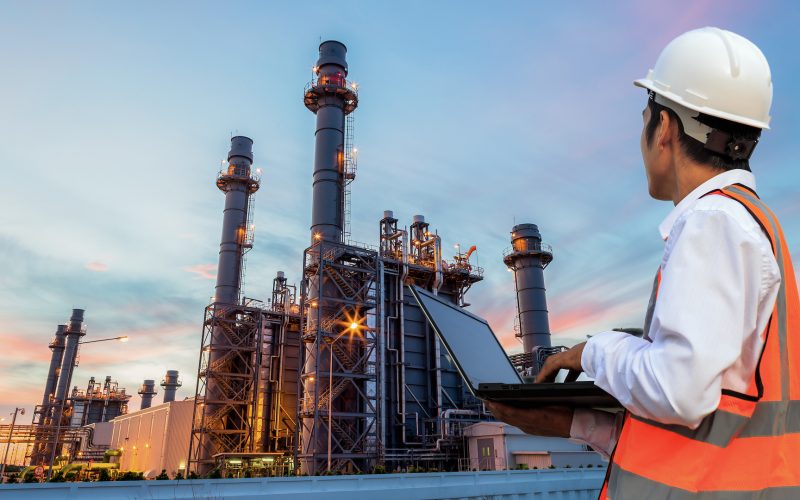 Engineering is use notebook check and standing in front of oil refinery building structure in heavy petrochemical industry